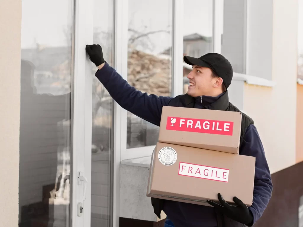 A Zenith delivery person wearing gloves and a cap knocks on a door while holding two boxes labeled "FRAGILE.