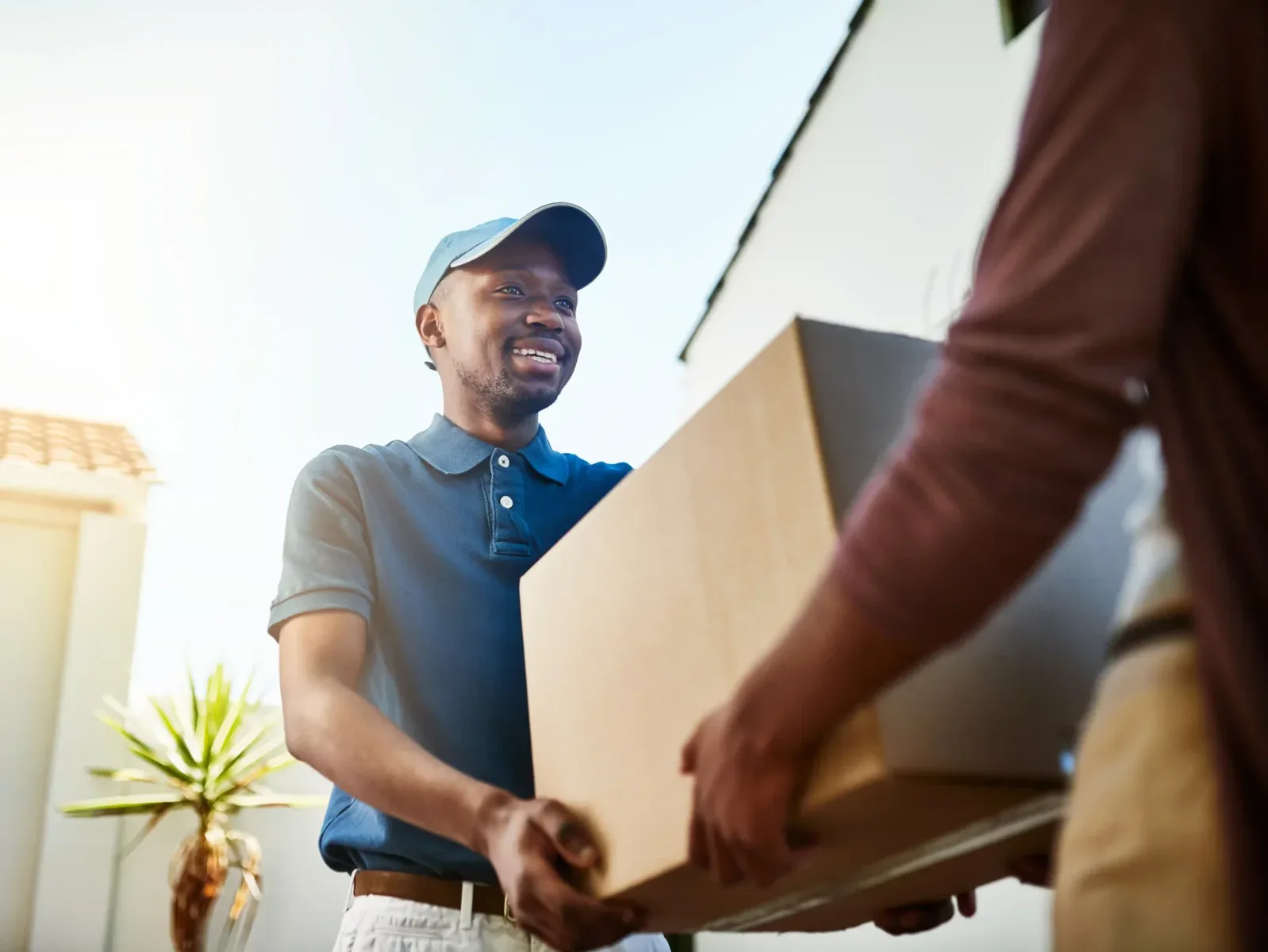 A delivery person in a blue shirt and cap hands a large cardboard box to another person outside a building, showcasing the reliable service offered by Zenith Moving Group for big moves and long-distance moving services.